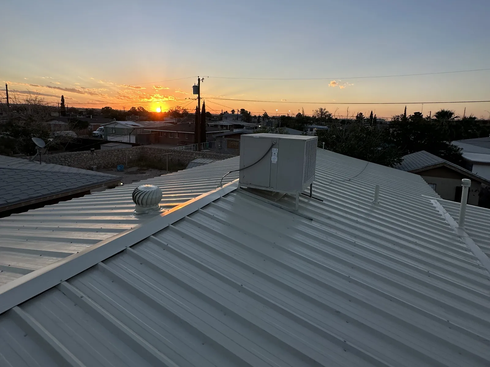 Finished Light Stone R-panel roof on an El Paso home at sunset, with a turbine vent and a swamp cooler