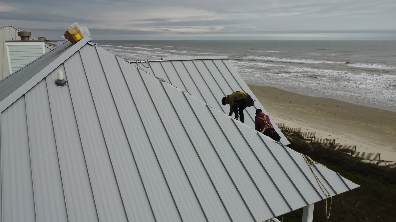 Crew installing standing seam panels on a beachfront home, the Gulf of Mexico behind